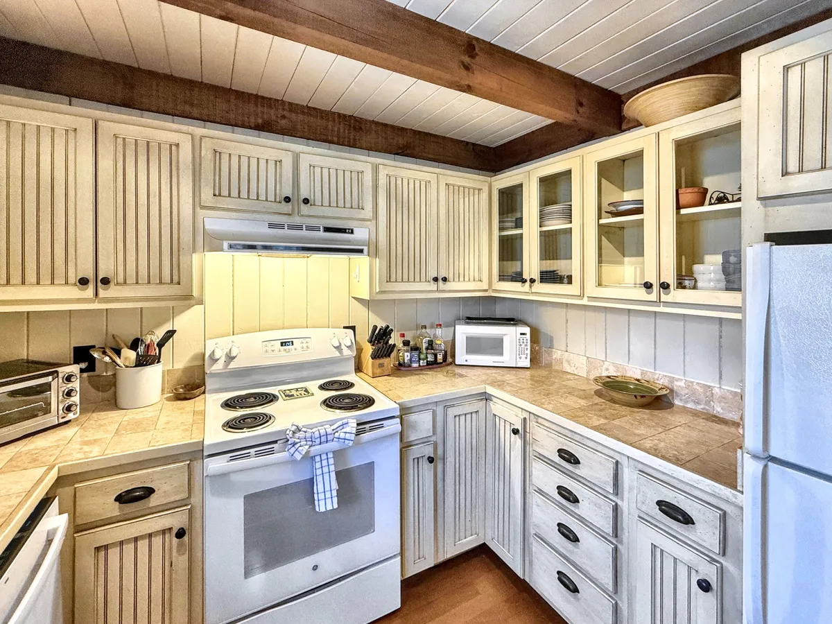 The image features a cozy and functional kitchen with a stove, kitchen cabinets, countertop, microwave, and sink. The scene is set for cooking and meal prep, with enough space for multiple people to gather and share in the experience.