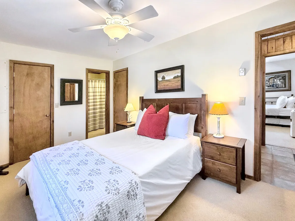 A tranquil bedroom scene with a bed decorated with patterned pillows and a soft quilt, flanked by nightstands and lamps, and accented by framed artwork and wooden doors. Natural light streams in, creating a peaceful and relaxing environment ideal for private escapes.