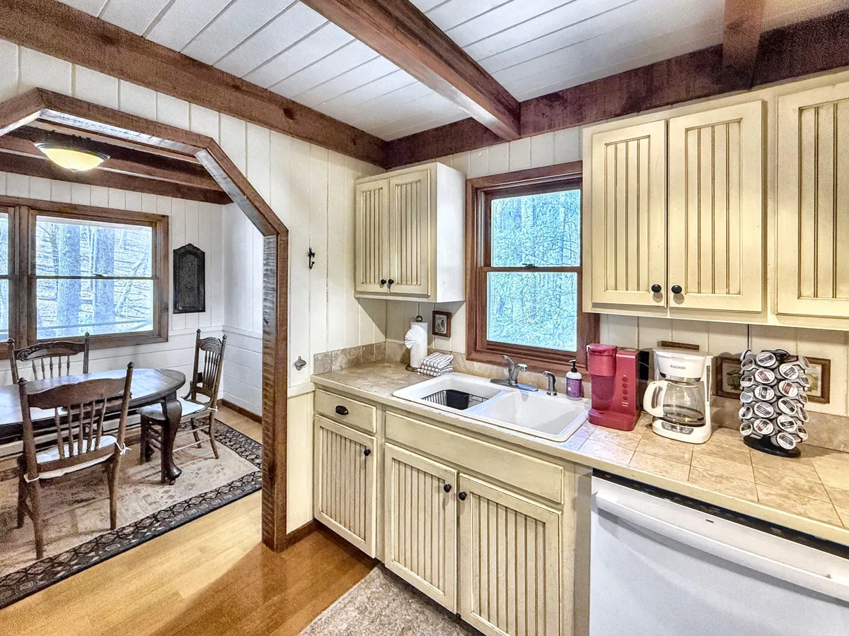 The image highlights the kitchen sink, dining table, and windows that let in natural light. The space feels open and inviting, ideal for shared meals and entertaining guests while connecting with the scenic outdoors.