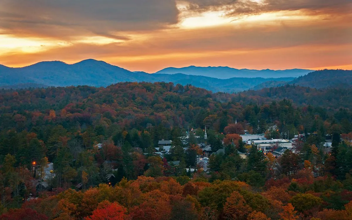 A sweeping view of vibrant fall foliage, distant mountains, and a small town nestled in a picturesque valley. The scene exudes serenity while underscoring the region’s scenic beauty and opportunities for exploration and relaxation.