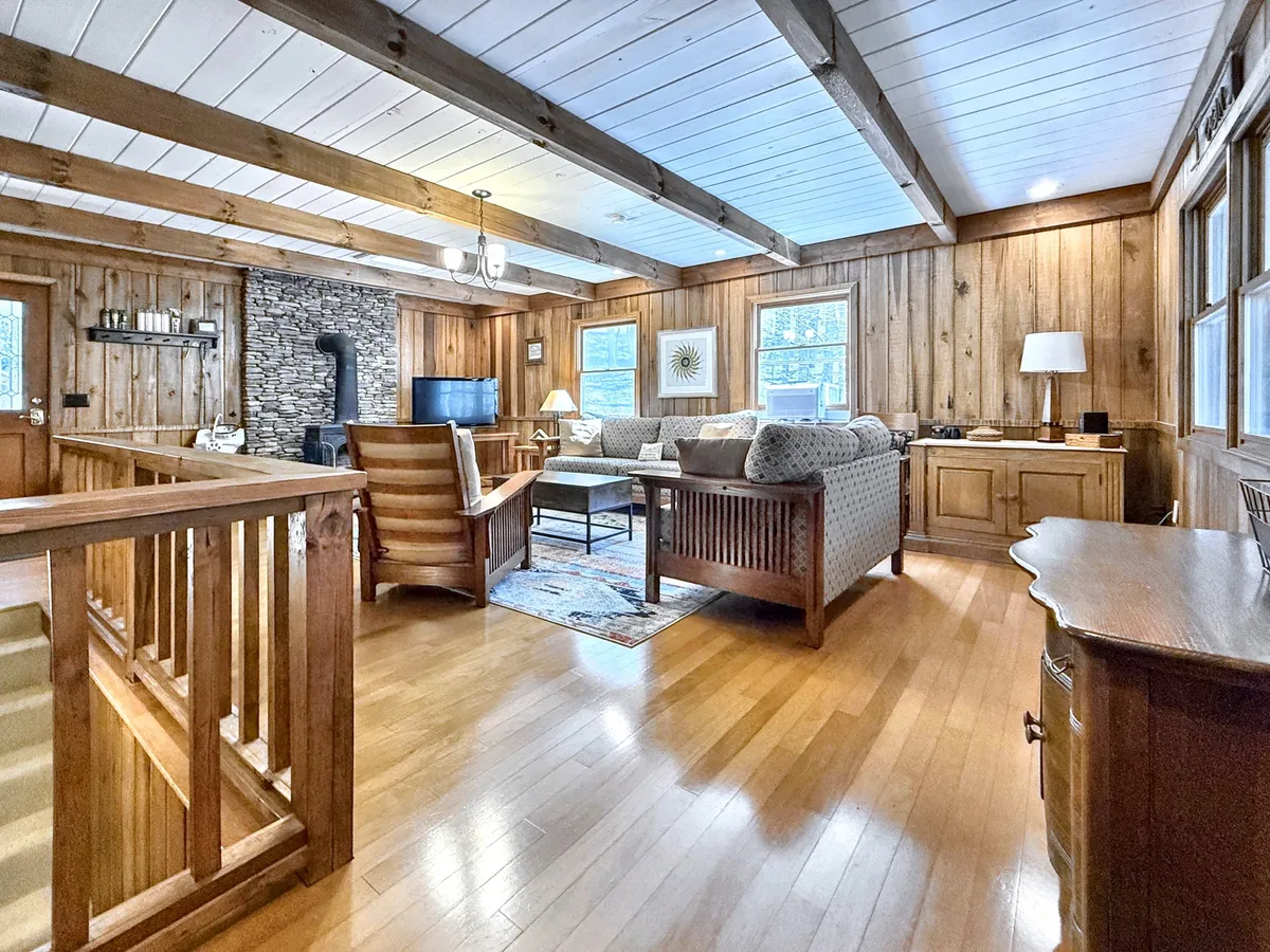 A warm, inviting living room featuring exposed wooden beams, a charming stone fireplace, comfortable seating, and wooden furniture. The scene is set for relaxing family time, entertaining guests, or curling up with a book by the fire. The arrangement is perfect for cozy gatherings and shared stories.