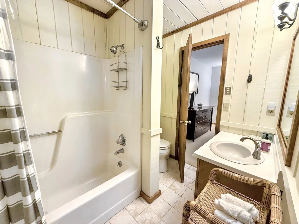 A tasteful bathroom with a bathtub and shower combination, a sleek vanity sink, and a woven basket stocked with towels. The space is practical yet inviting, with subtle decorative touches and soft lighting that enhance relaxation.