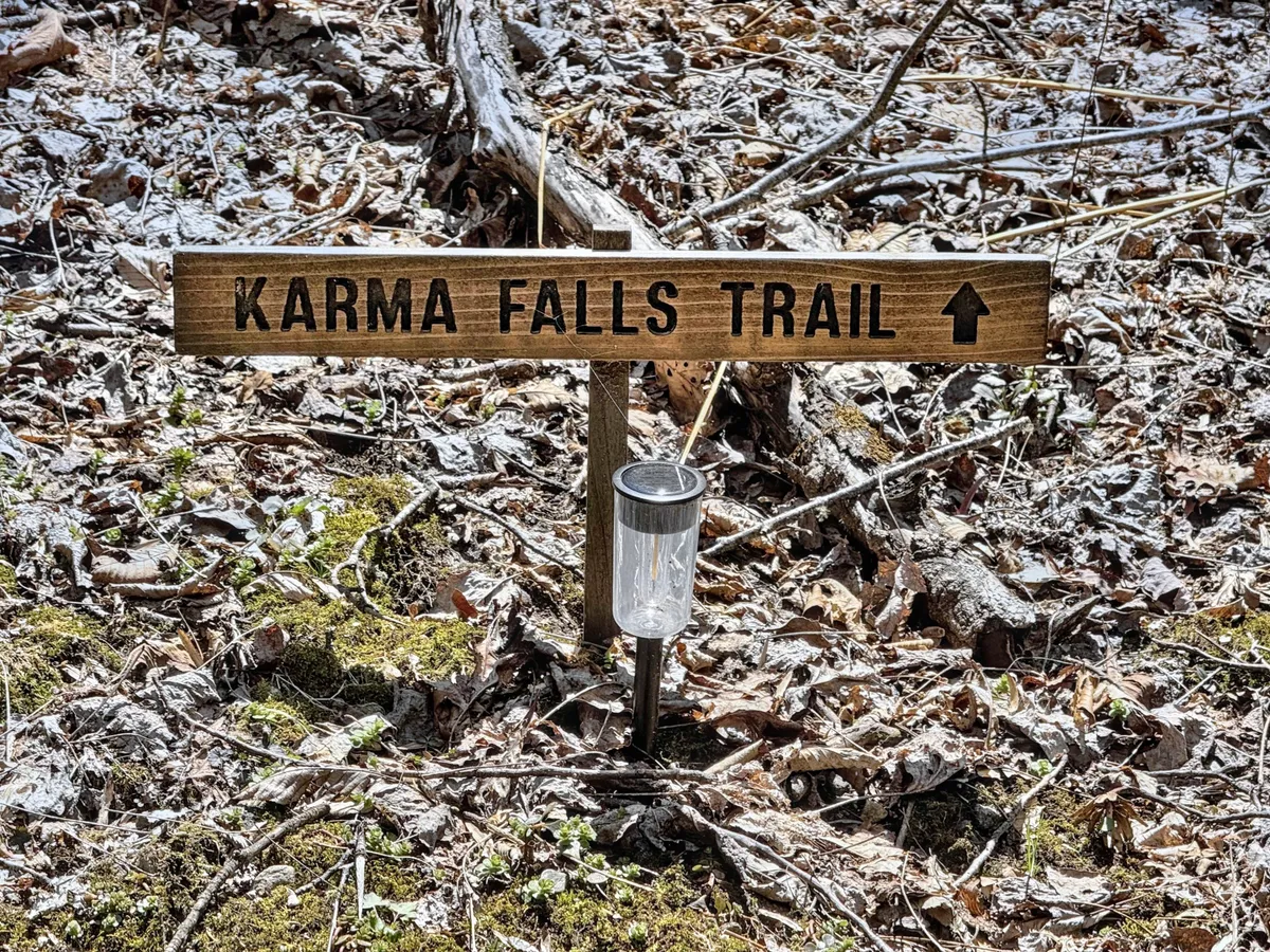A rustic wooden sign marks the entrance to a nature trail, illuminated by a solar light. The scene suggests the start of an outdoor adventure, with surrounding greenery hinting at the untamed beauty waiting to be explored.